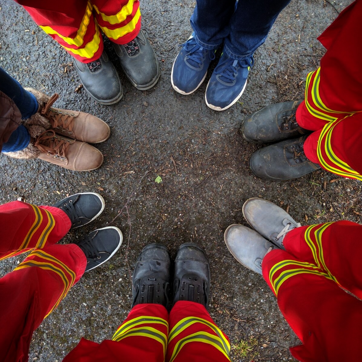 Beine und Füße von 7 Personen, die im Kreis stehen. 5 davon Tragen eine DLRG-Einsatzhose.